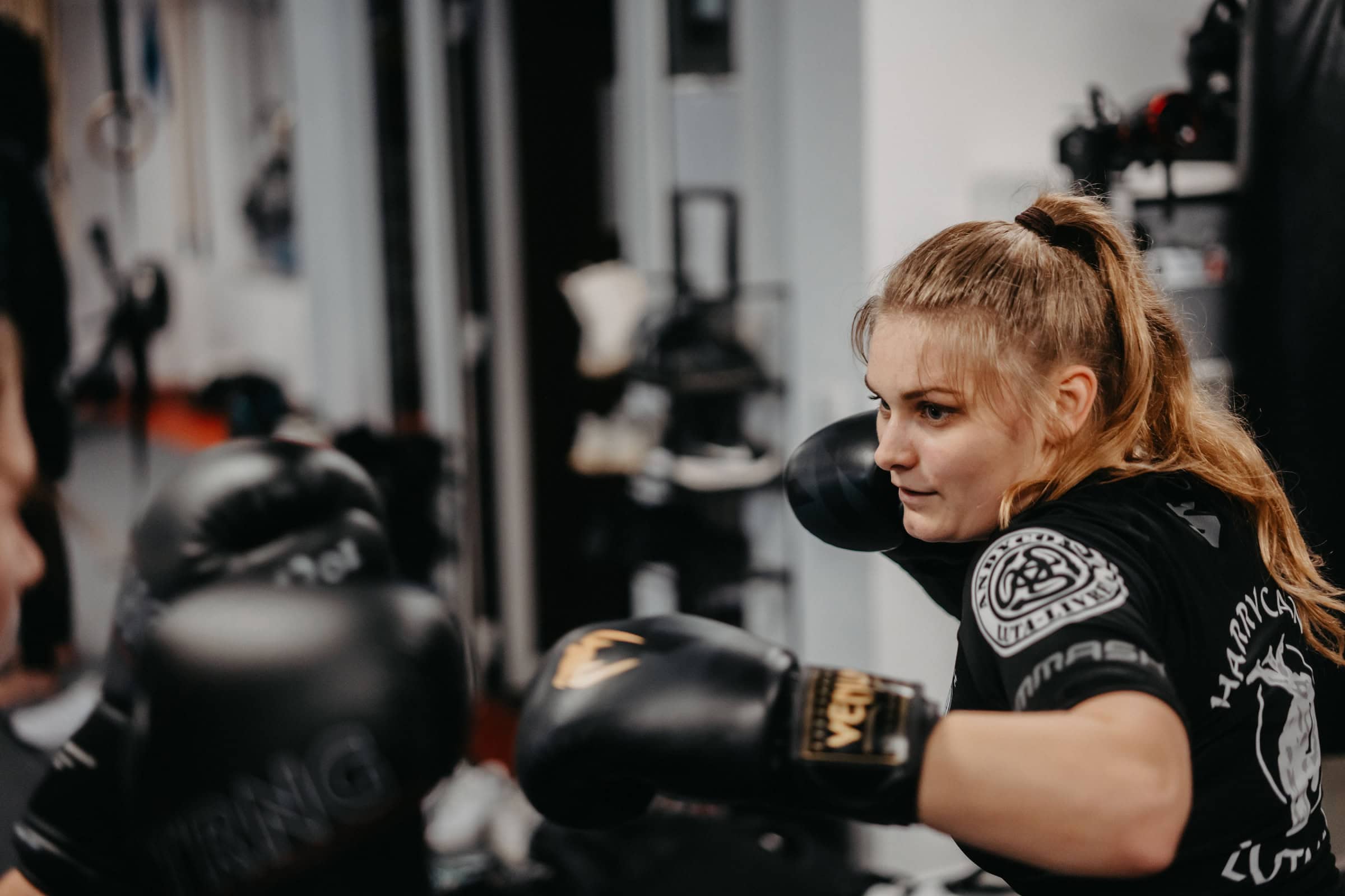 Fokussierte Trainerin von Harrycane Luta Livre beim Boxtraining mit schwarzen Handschuhen im Trainingsraum.