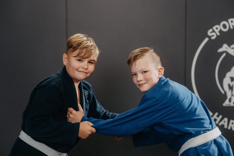 Zwei Jungen im Kindertraining bei Harrycane Luta Livre, üben Grifftechniken in blauen Gi-Trainingsanzügen.